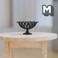 1:12 scale miniature large metal wire fruit basket in black with pedestal foot, shown on a round wood table
