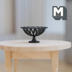 1:12 scale miniature large metal wire fruit basket in black with pedestal foot, shown on a round wood table