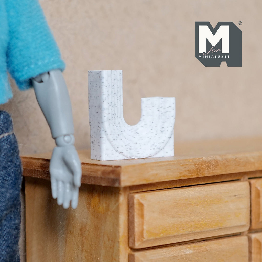 1:12 scale miniature white marble look double neck vase in a U shape, shown on a wood dresser beside a figure's hand
