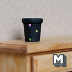 1:12 scale miniature black ceramic round polka dot flower pot, tapered with rim, shown on a wood dresser