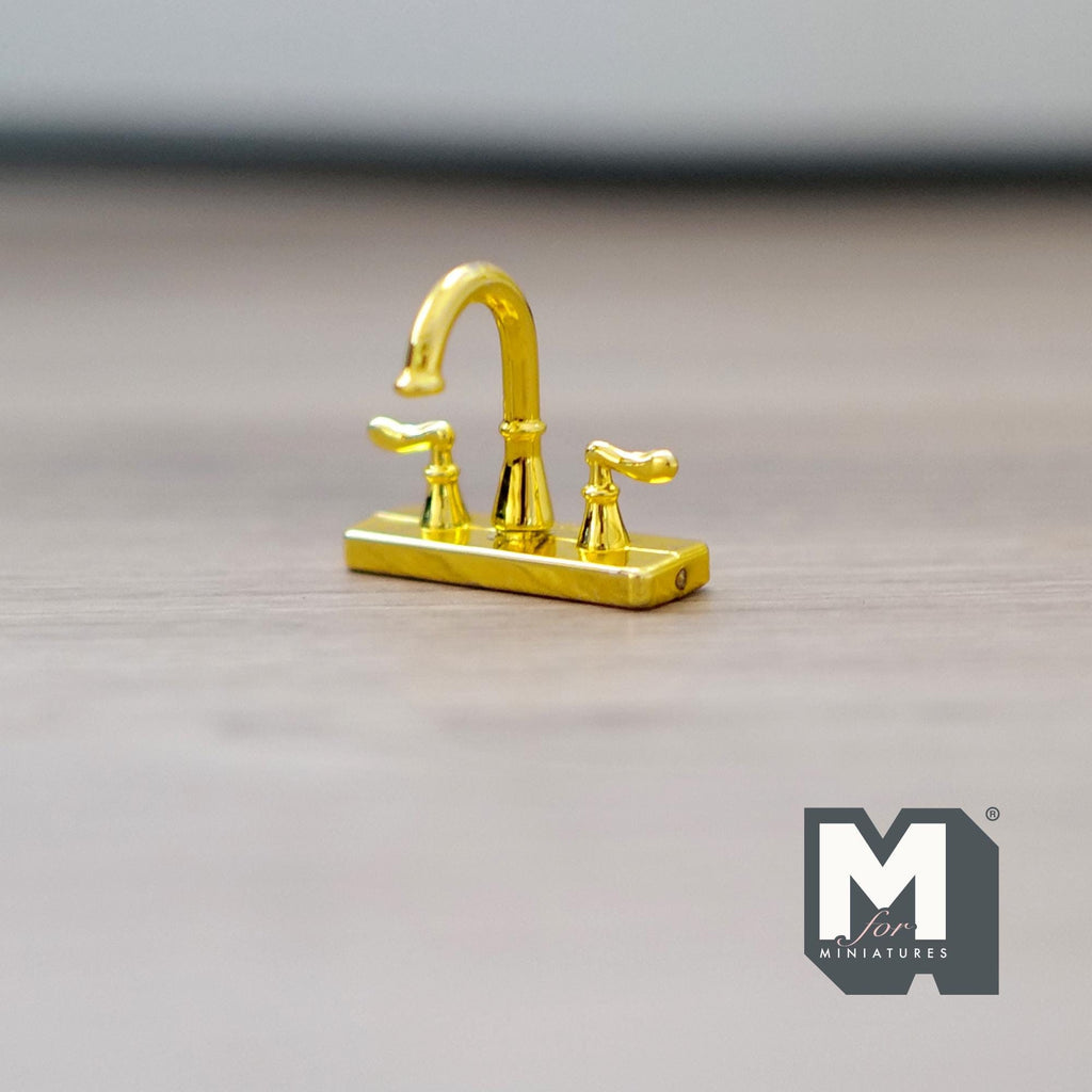1:12 scale miniature widespread faucet in gold with double handles and arched spout, shown on a wood surface
