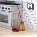 1:12 scale miniature red metal broom and long handle dustpan set, shown leaning beside a kitchen stove