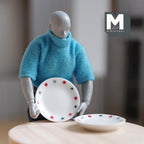 1:12 scale miniature large ceramic polka dot plates in white with red and green dots, set of 2, held by a figure