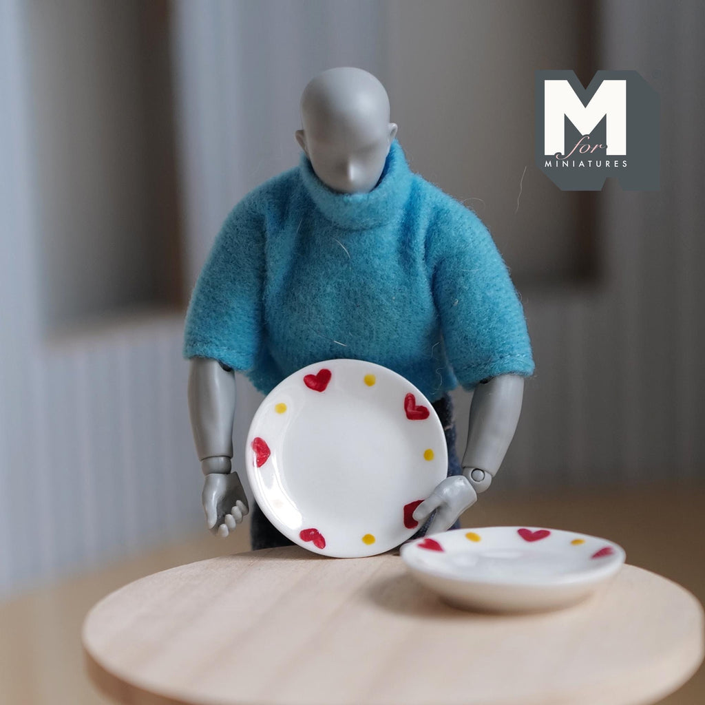 1:12 scale miniature large ceramic plates in white with red heart rim, set of 2, held by an artist figure