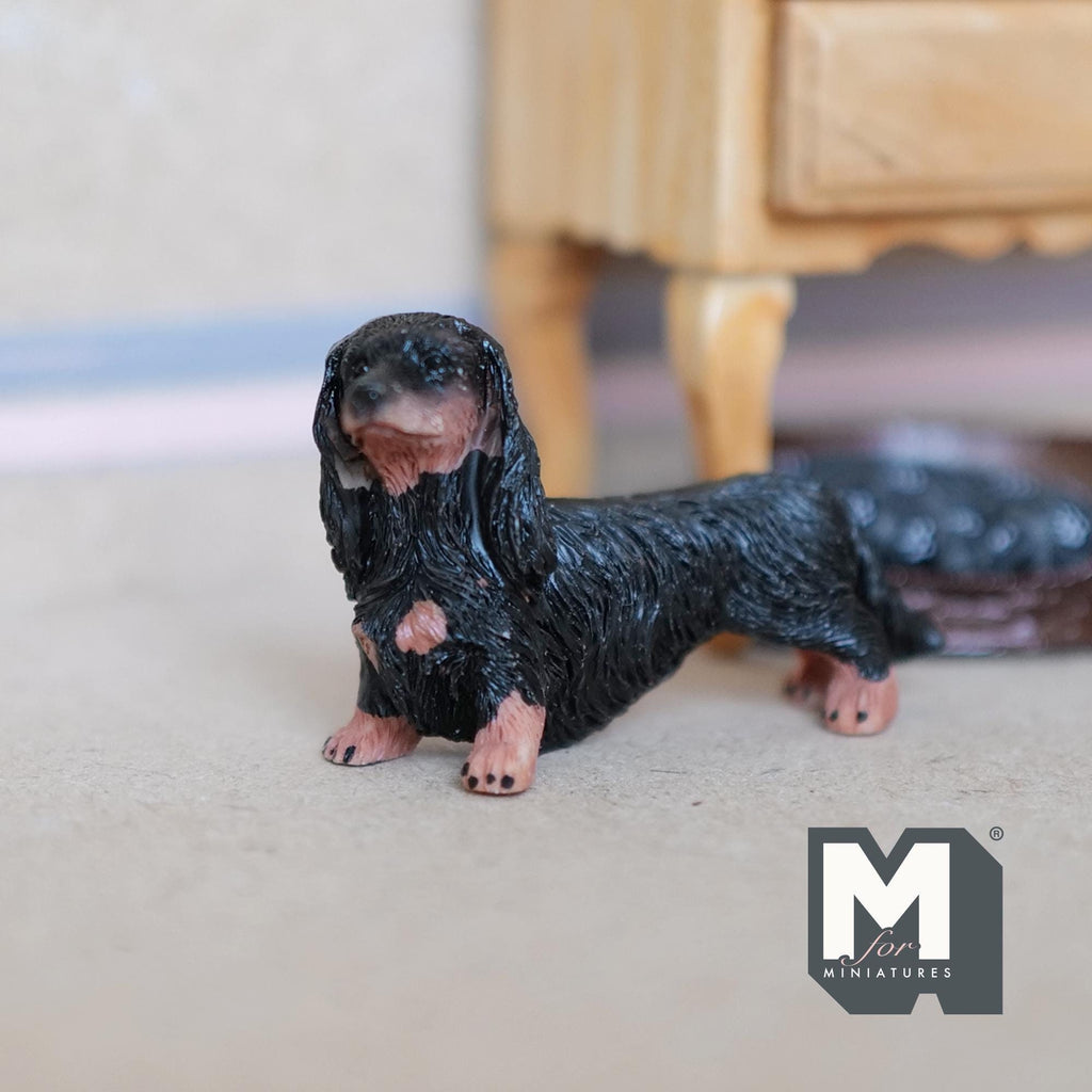 1:12 scale miniature cast resin standing long hair dachshund puppy in black and tan, shown beside a wood cabinet