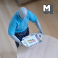 1:12 scale miniature ceramic serving tray with handles, gold rim and floral center, held by a poseable figure