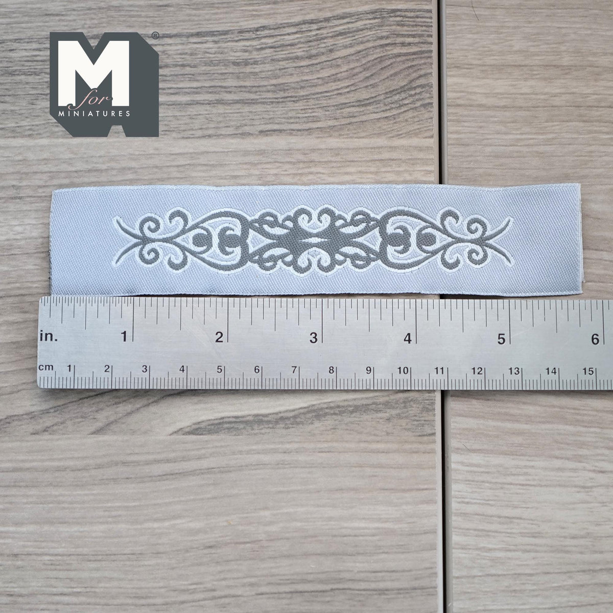 1:12 scale miniature white lace style table runner with scroll cutout pattern, shown with a ruler on a wood floor