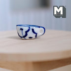 1:12 scale miniature ceramic cream boat with handle, white with hand painted blue pattern, shown on a round wood table