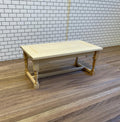 1:12 scale miniature unpainted wood dining table with turned legs and stretchers, shown on a wood floor by a white tile wall