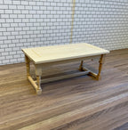 1:12 scale miniature unpainted wood dining table with turned legs and stretchers, shown on a wood floor by a white tile wall