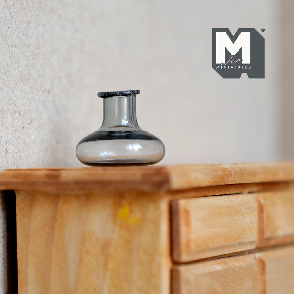 1:12 scale miniature gray glass bottle vase with squat round body and short neck, shown on a wood dresser