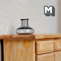1:12 scale miniature gray glass bottle vase with squat round body and short neck, shown on a wood dresser