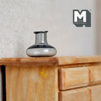 1:12 scale miniature gray glass bottle vase with squat round body and short neck, shown on a wood dresser