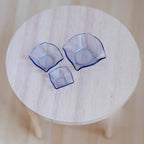 1:12 scale miniature glass mixing bowls in light blue, set of 3 assorted sizes with wavy rims, on a round wood table