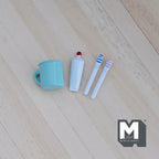 1:12 scale miniature aqua toothbrushes, toothpaste and rinse cup, set of 4, laid out on a light wood surface