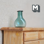 1:12 scale miniature glass bottle vase in teal with round body and narrow neck, shown on a wood dresser