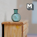 1:12 scale miniature green glass bottle vase with round body and short neck, translucent teal green, on a wood cabinet