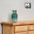 1:12 scale miniature green glass bottle vase with wide short neck, translucent teal green, on a wood dresser