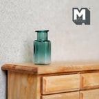 1:12 scale miniature green glass bottle vase with wide short neck, translucent teal green, on a wood dresser