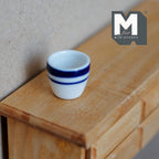 1:12 scale miniature white ceramic planter bowl with blue striped rim, tapered cup shape, shown on a wood dresser
