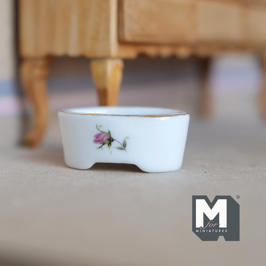 1:12 scale miniature white oval ceramic planter with feet, gold rim and pink floral decal, shown on a carpet