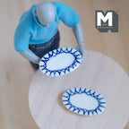1:12 scale miniature ceramic oval plates in white with blue zigzag rim, set of 2, held by an artist figure