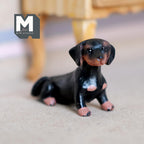 1:12 scale miniature cast resin lying dachshund puppy in black and brown, shown on a carpeted floor