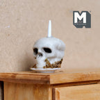 1:12 scale miniature skull cake in cast resin with a white candle on a plate, shown on a wood nightstand