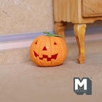 1:12 scale miniature clay jack o lantern pumpkin in orange with a toothy grin, style B, shown on a floor by a table leg