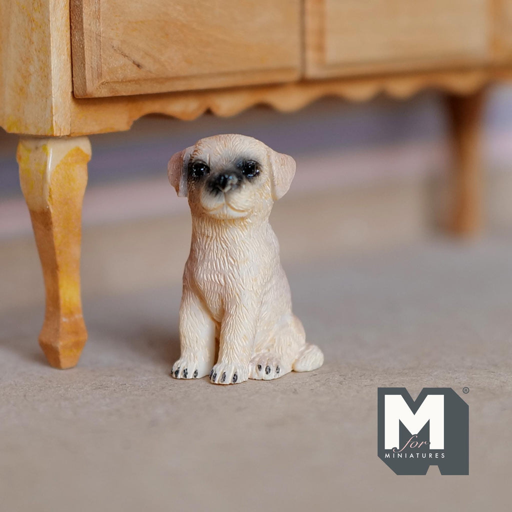 1:12 scale miniature cast resin sitting Labrador puppy in cream with dark muzzle, shown beside a wood cabinet leg