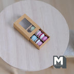 1:12 scale miniature box of macarons, 8 pieces in pastel pink, blue and green, shown in a kraft window box on a table