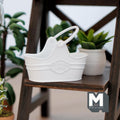1:12 scale miniature metal flower basket in white with arched handle and embossed emblem, shown on a dark wood plant stand