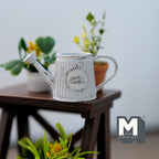 1:12 scale miniature metal slanted watering can in light blue with ribbed body and rustic label, on a wood plant stand
