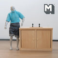 1:12 scale miniature unpainted wood kitchen sink cabinet with 2 doors and black taps, shown beside a figure for scale