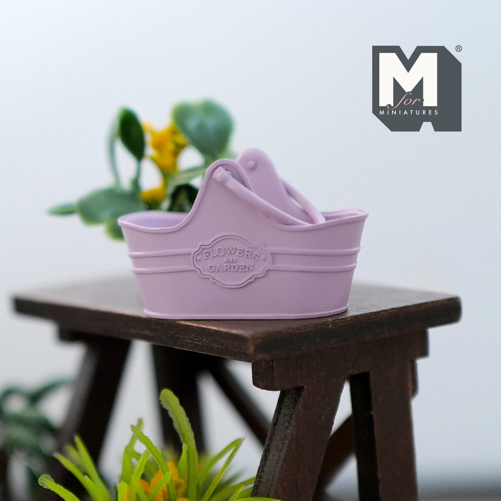 1:12 scale miniature metal flower basket in purple with arched handle and embossed emblem, on a dark wood stool