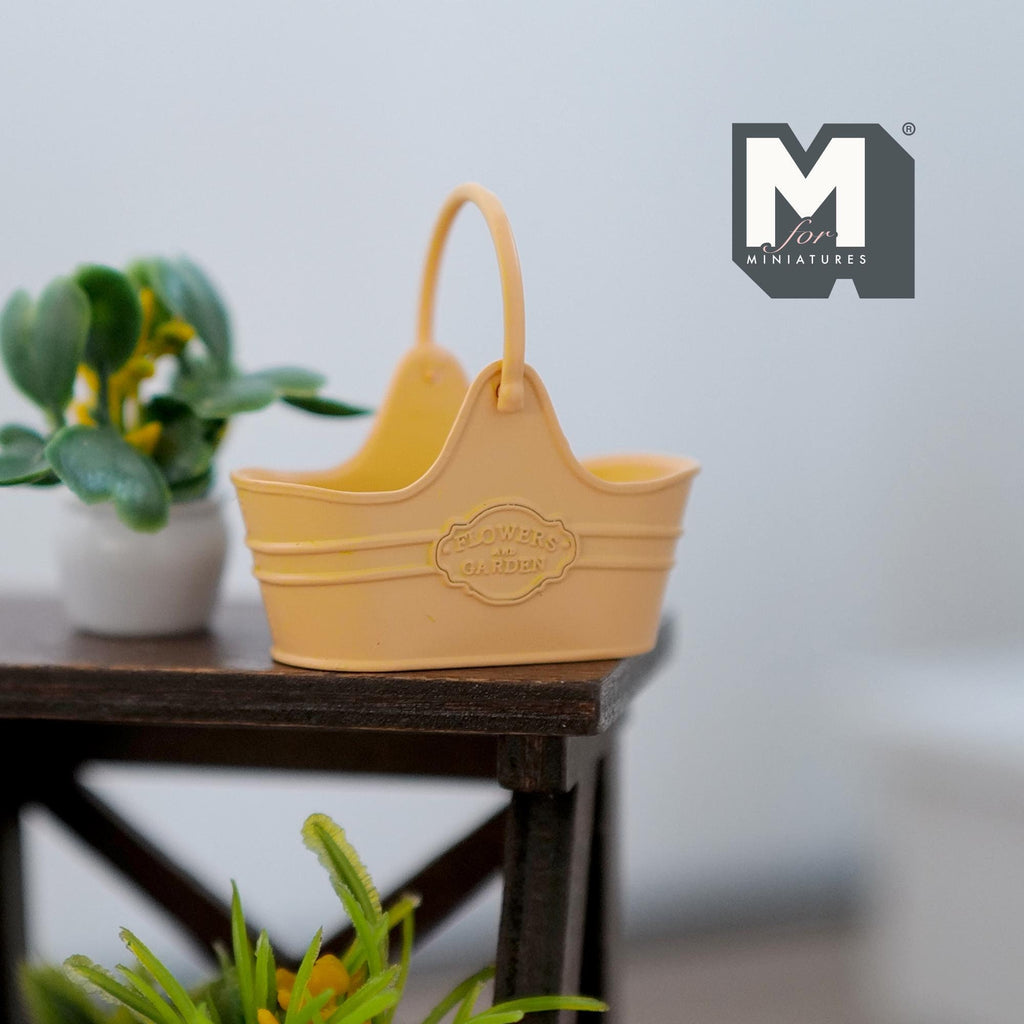 1:12 scale miniature orange metal flower basket with arched handle, shown on a dark wood plant stand beside a plant