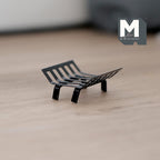 1:12 scale miniature metal fire grate in black with curved slatted bars and four legs, shown on a light wood floor