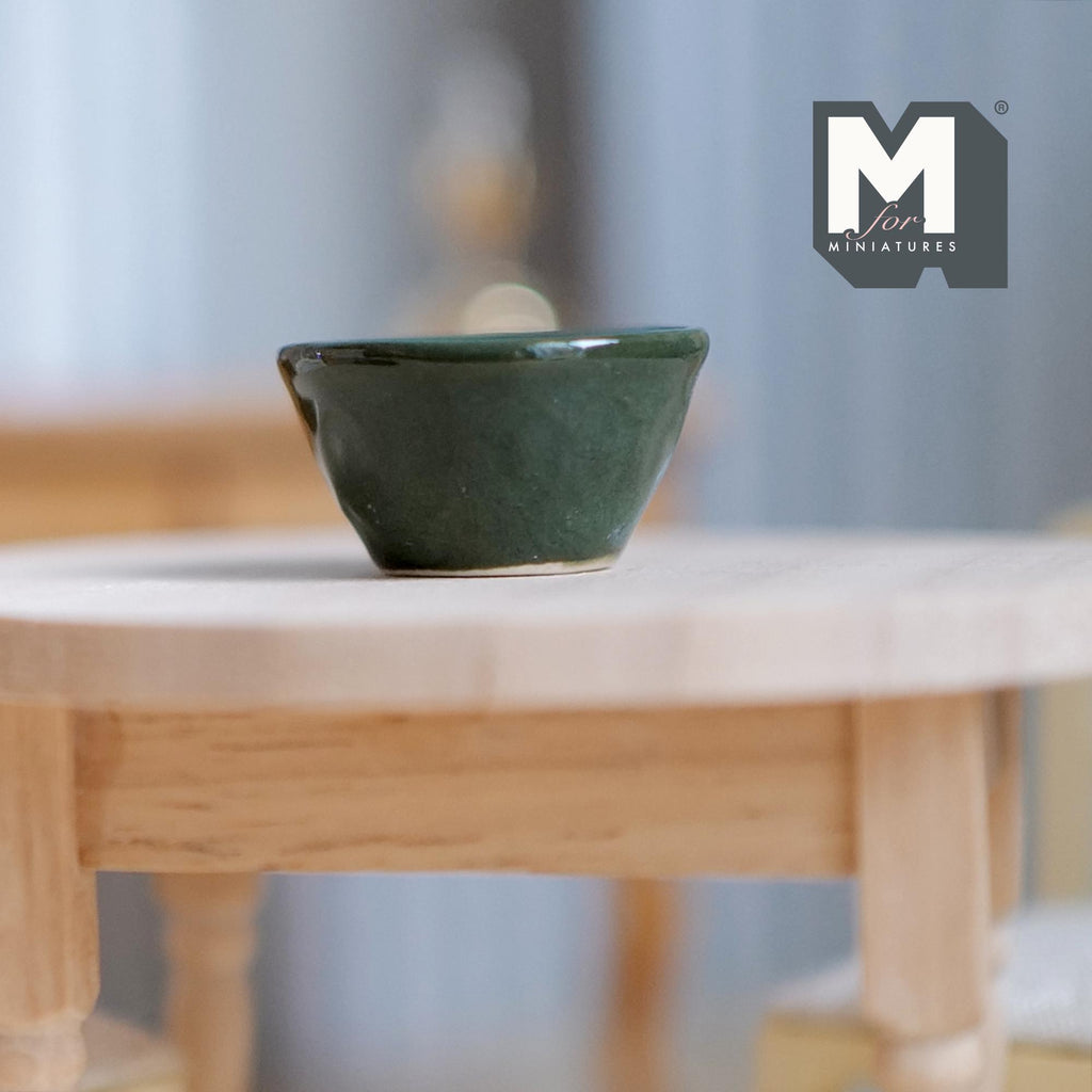 1:12 scale miniature dark green ceramic fruit bowl with glossy glaze, shown on a light wood table