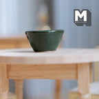 1:12 scale miniature dark green ceramic fruit bowl with glossy glaze, shown on a light wood table