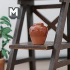 1:12 scale miniature clay plum shaped vase in reddish brown with clear coat top, shown on a dark wood shelf