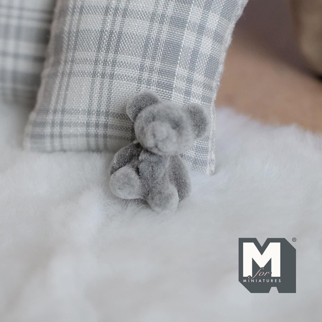 1:12 scale miniature gray teddy bear cub with flocked skin, sitting on a white fur rug beside a plaid pillow