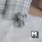 1:12 scale miniature gray teddy bear cub with flocked skin, sitting on a white fur rug beside a plaid pillow