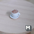 1:12 scale miniature latte coffee cup with saucer, white cup with latte art foam, shown on a round wood table
