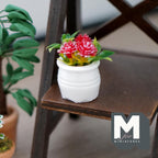 1:12 scale miniature potted flowering plant with red blooms and green leaves in a round white pot, shown on a dark wood shelf
