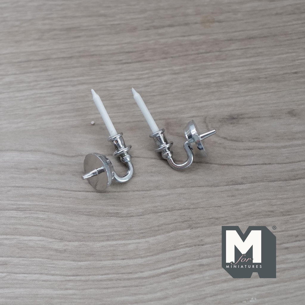 1:12 scale miniature metal wall candle sconces in silver with white candles, set of 2, lying on a wood surface
