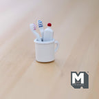 1:12 scale miniature white rinse cup with toothbrushes and toothpaste, set of 4, red and blue brushes, on a wood surface