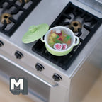 1:12 scale miniature vegetable soup in a green metal pot with lid, shown on a kitchen stove top