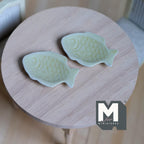 1:12 scale miniature ceramic fish shaped plates in pale green, set of 2, shown on a round wood table