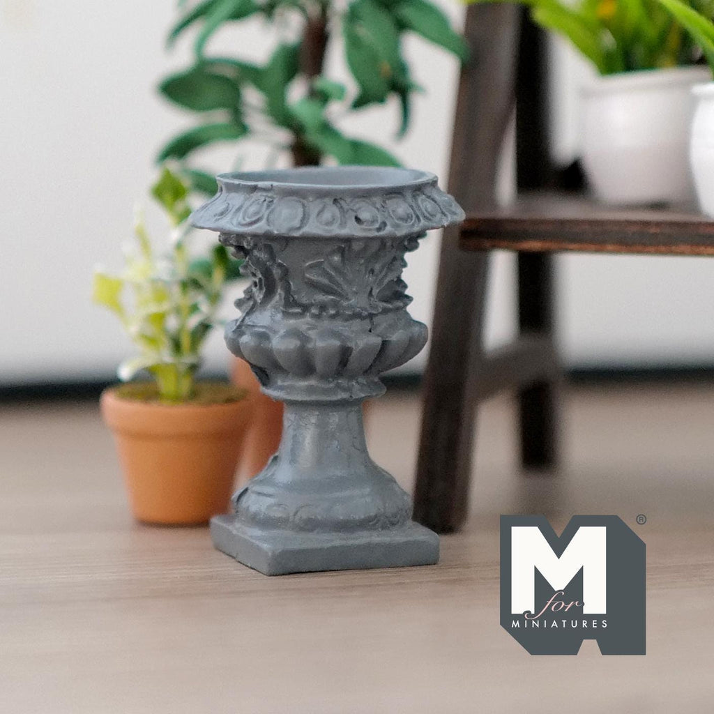 1:12 scale miniature Roman style pedestal urn vase in gray cast resin with fluted sides, shown beside potted plants