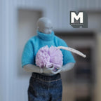 1:12 scale miniature shower loofah in purple with a white hanging cord, held by an artist figure